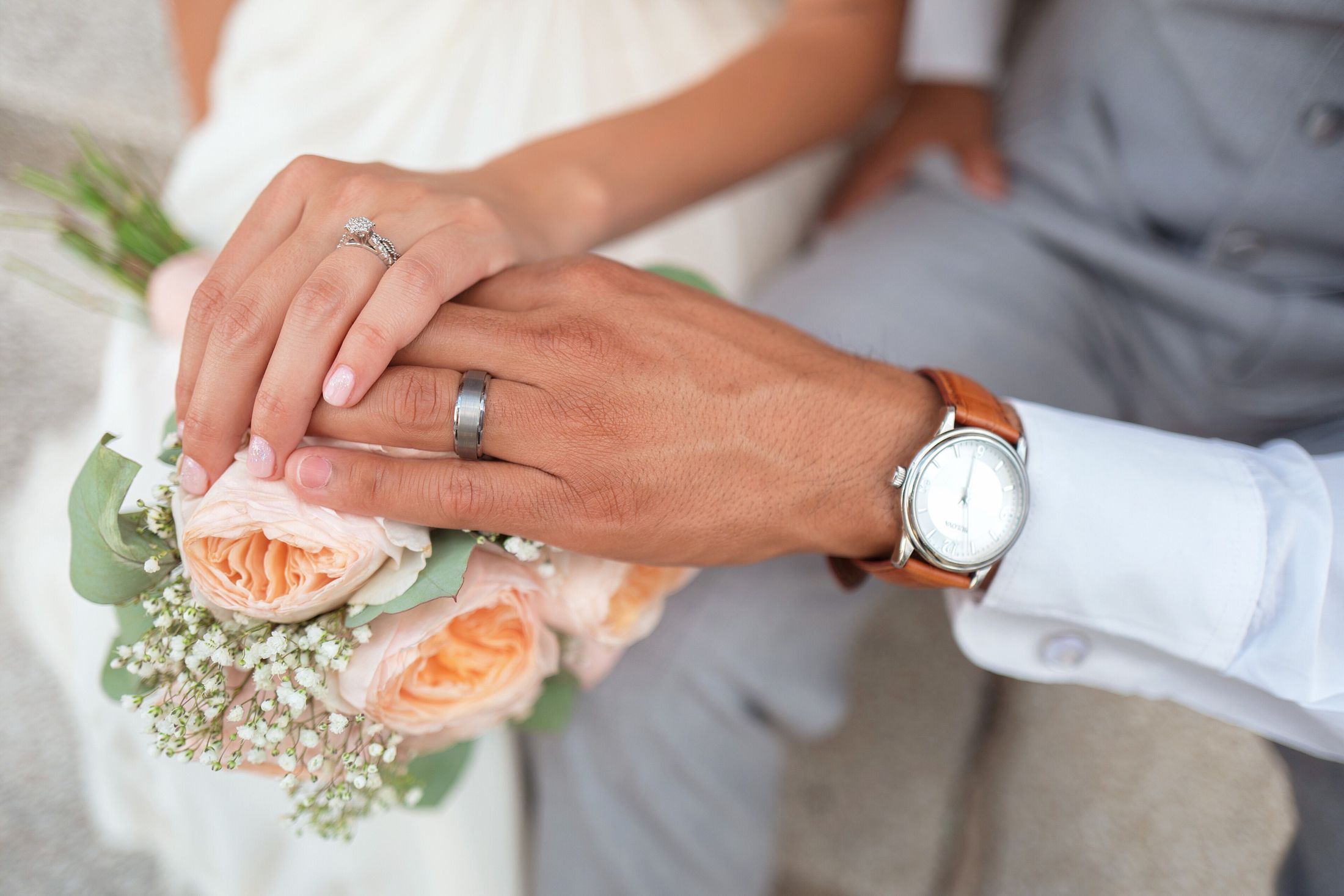 A bride and groom holding hands over a bouquet